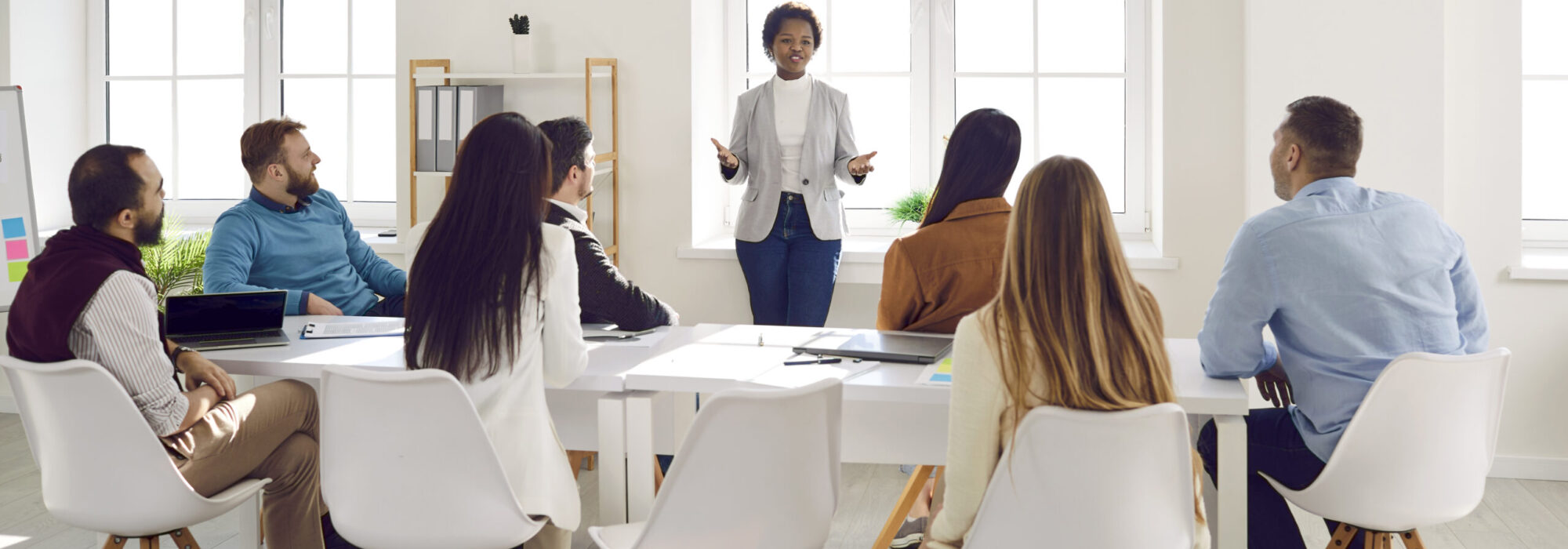 Young Black female team leader speaking to business people sitting around office table